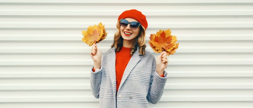 Autumn portrait of beautiful happy smiling woman with yellow maple leaves in red french beret hat and glasses posing on white background