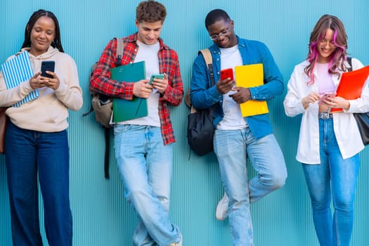 Smiling multiracial teenagers browsing the internet with mobile phones on college campus standing in blue background