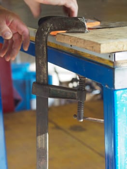 Carpenter is using a g clamp to secure wood to a workbench for cutting. The image shows the importance of safety and precision in carpentry