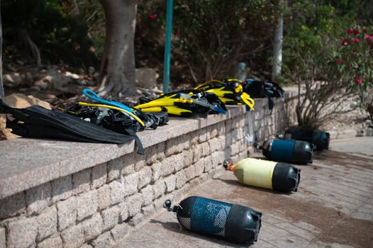 A collection of scuba diving gear, including tanks and fins, arranged on a stone wall at the beach, ready for an underwater adventure.