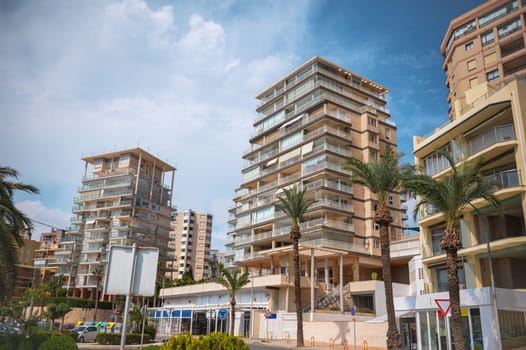 Urban scene featuring modern apartment buildings with balconies, surrounded by palm trees, under a bright blue sky. Ideal for real estate or cityscape themes.