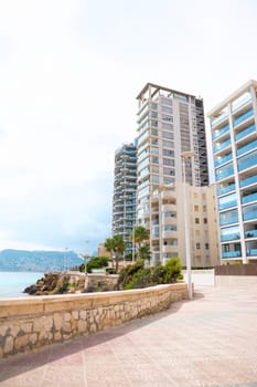 Contemporary high-rise buildings tower along a picturesque beachfront promenade, showcasing stunning architectural design with a serene atmosphere under a bright blue sky.