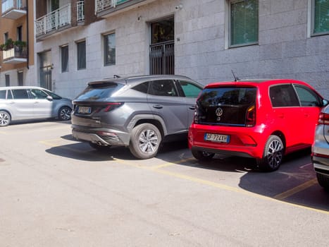 Cremona, Italy August 31st 2024 Neatly parked cars in a residential area on a sunny day, lined up parallel in an empty lot with buildings in the background
