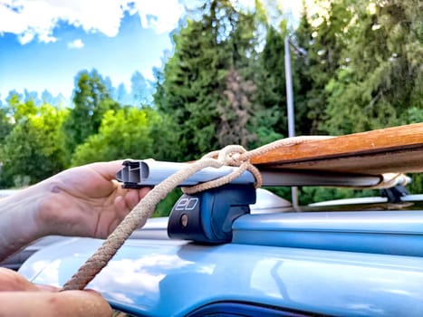 A hand secures wooden planks to a vehicle roof, ideal for travel, adventures, and outdoor activities