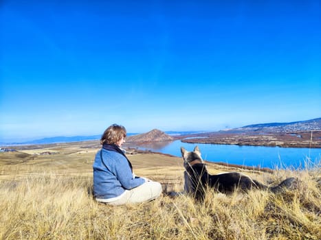 A woman and her German Shepherd enjoy a hike overlooking a picturesque lake on a clear sunny spring morning