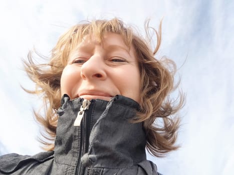 A middle-aged woman smiles broadly while traveling outdoors with a clear sky above her. The adventures of a middle-aged female tourist on trip