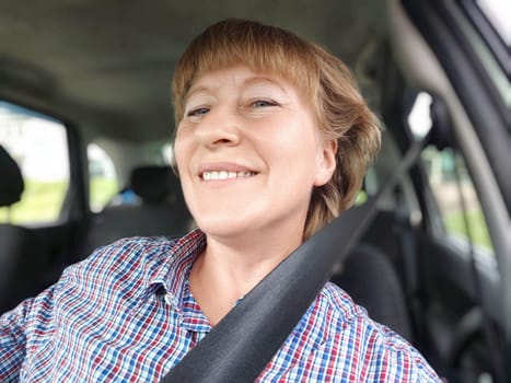 Middle aged woman is seated in a car, smiling cheerfully as she securely fastens her seat belt. Safety in transport. Traffic Laws