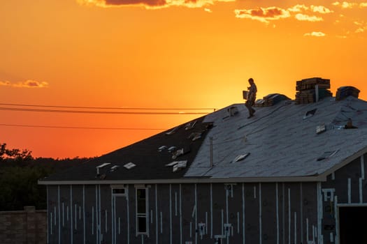 Georgetown, TX - 3 October 2024: Roofing contractor carrying shingles for roofing new home late in evening at sunset