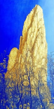 Golden rock formation towers over bare trees under a vibrant blue sky, showcasing nature's beauty in the southwest usa