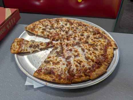 Honolulu - August 15, 2024: A freshly baked pizza sits on a metal tray, with a few slices taken, ready to be enjoyed at a lively Chuck E. Cheese venue in Hawaii.