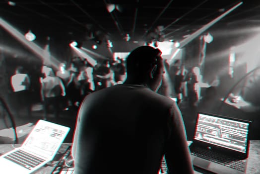back DJ in headphones mixing music on stage at a party in a nightclub. Black and white photo with glitch effect and small grain