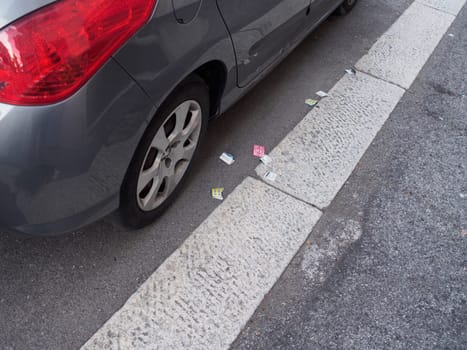 Cremona, Italy August 31st 2024 Grey car parked on an asphalt parking lot with several parking tickets scattered on the ground next to it
