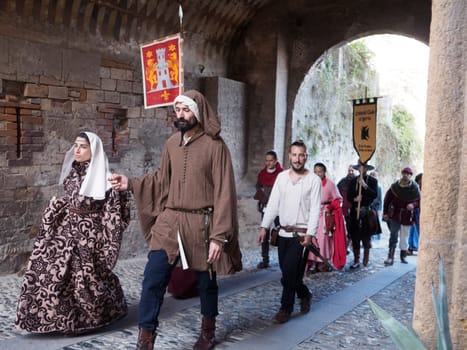 Castellarquato, Italy August 31st 2024 Medieval historical reenactors wearing traditional costumes are walking through an ancient stone archway in an italian village