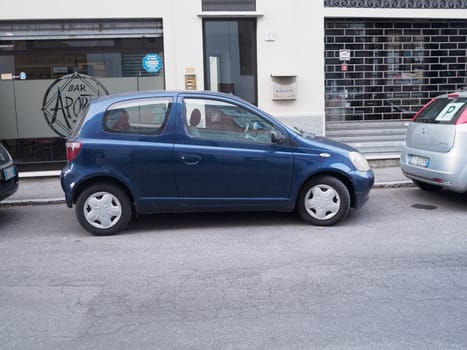Cremona, Italy August 31st 2024 A blue compact car is parked on the side of a city street, with a closed storefront in the background