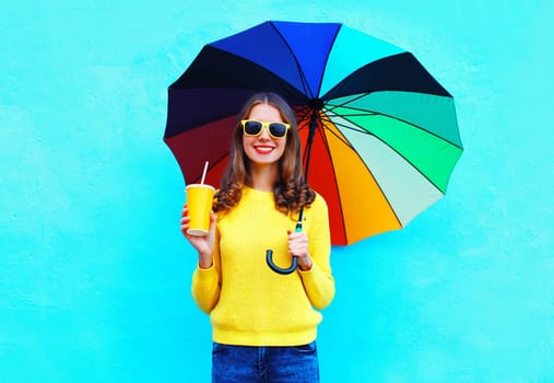 Fashion happy smiling young woman with juice cup, colorful umbrella in autumn day on blue background