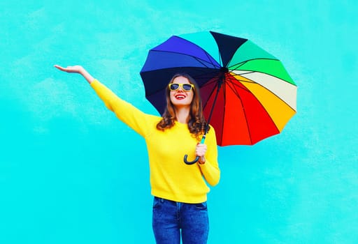 Happy smiling young woman holding colorful umbrella in autumn looking up on colorful blue background