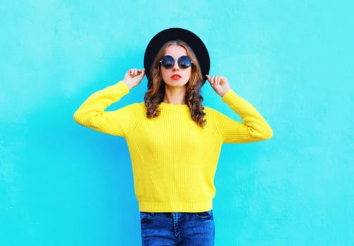 Fashion beautiful woman wearing a black hat, yellow knitted sweater on colorful blue background