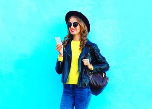portrait young woman using smartphone wearing a black rock style clothes on colorful blue background