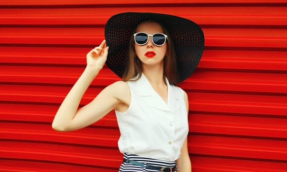 Portrait of stylish young woman model posing wearing black summer straw round hat on red background
