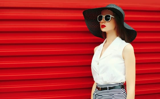 Portrait of stylish young woman model posing wearing black summer straw round hat on red background