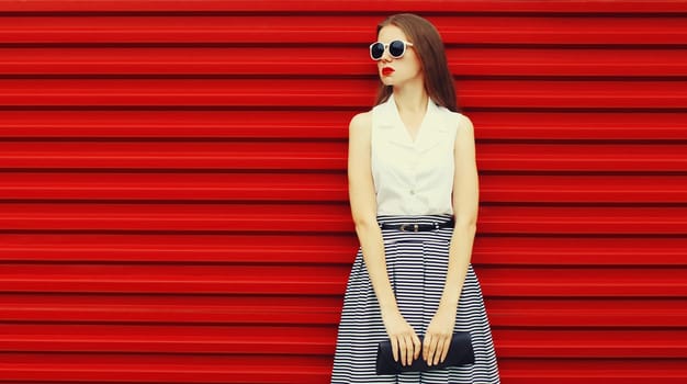 Portrait of stylish young woman model posing wearing skirt, handbag on red background