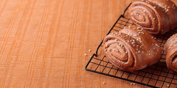 Korvapuusti, traditional finnish cinnamon and cardamom rolls, fresh baked buns on the metal grid, sweet dessert Sweden and Finland, horizontal banner with copy space