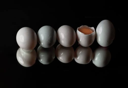 Five raw duck eggs are sitting in a row with an egg broken in half showing the yolk and white egg with reflection on dark background. use it as your Wallpaper, Poster and Space for text, Selective focus.