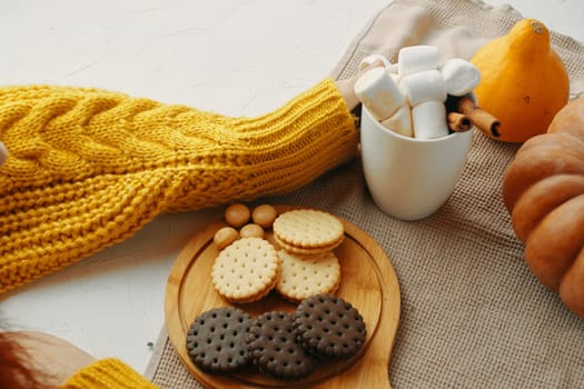 Cozy autumn scene with biscuits, marshmallows, yellow sweater, and pumpkins, offering a warm and inviting feel