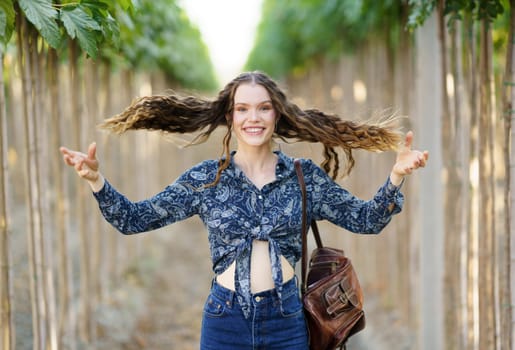 A cheerful young woman showcases her long, beautiful hair while playfully posing in a picturesque treelined path, radiating happiness, confidence, and a carefree spirit, embodying joy and adventure