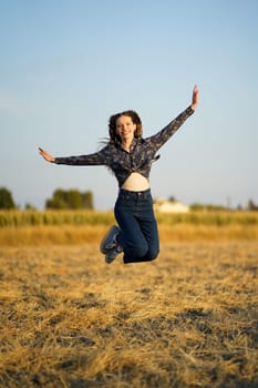 A cheerful and spirited young woman leaps joyfully and exuberantly in a sunlit golden field, embodying the essence of freedom and pure happiness against a serene and picturesque backdrop