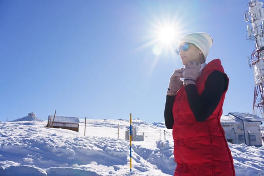Low angle of determined sportive lady in outerwear and sunglasses putting on headphones standing in sunny winter terain