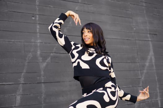 Expressive female hispanic modern dancer smiling while performing in the city next to grey wall