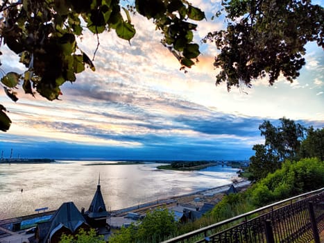 The sun sets beautifully over the river, casting colors across the sky while trees frame the tranquil scene of water and land.
