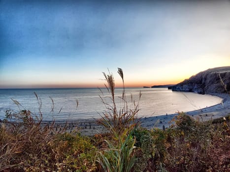 The sun sets behind a calm beach, casting warm colors across the water and creating a peaceful ambiance.