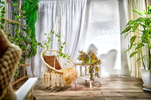 Modern cozy beautiful room with a braided rope macrame chair, green plants, small table and curtains. Interior and background. Location for photo shooting