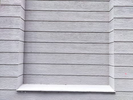A plain gray wooden wall with distinct textures and a window frame featuring a small ledge.