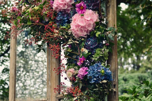 Pink, blue hydrangea, red berries, green leaves in decorations on a wooden window in a garden