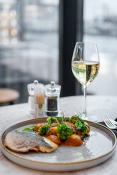 Sea bass or dorado fillet with baked potatoes and cauliflower on a gray plate on a marble table in a restaurant