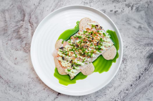 Shrimp tartare with sesame sauce and wasabi cream on a white plate on a marble table in a restaurant