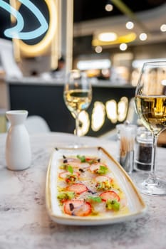 Sea bass ceviche with strawberry, kiwi and mango salsa on a marble table in a restaurant and a glass of white wine