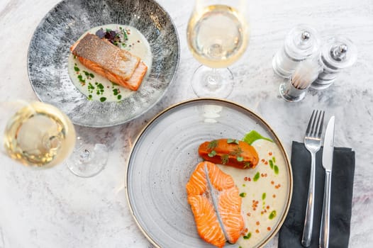 Two plates of salmon fillet in cream sauce with herbs on a marble table in a restaurant. High quality photo