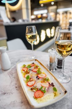 Sea bass ceviche with strawberry, kiwi and mango salsa on a marble table in a restaurant and a glass of white wine