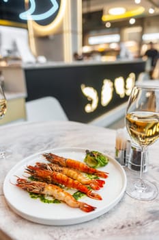 Langoustines with spinach sauce on a white plate on a marble table with a glass of white wine. High quality photo