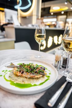 Sea bass in cream sauce with Provencal herbs and green olive oil on a white plate on a marble table in a restaurant