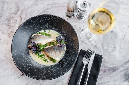 Sea bass in cream sauce with spinach and green oil on a black plate on a marble table in a restaurant