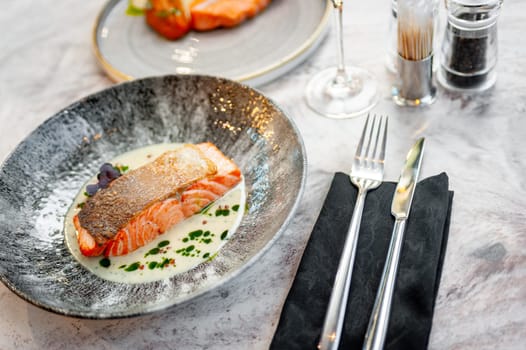 Salmon fillet in cream sauce with herbs on a marble table in a restaurant. High quality photo