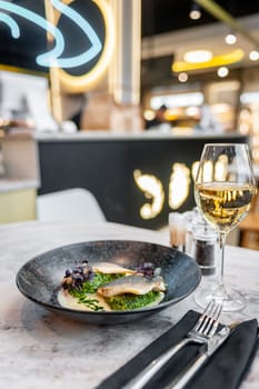 Sea bass in cream sauce with spinach and green oil on a black plate on a marble table in a restaurant