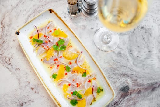 Sea bass ceviche with orange and mango salsa on a marble table in a restaurant and a glass of white wine