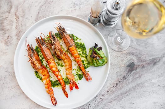 Langoustines with spinach sauce on a white plate on a marble table with a glass of white wine. High quality photo