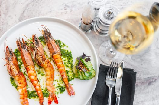 Langoustines with spinach sauce on a white plate on a marble table with a glass of white wine. High quality photo